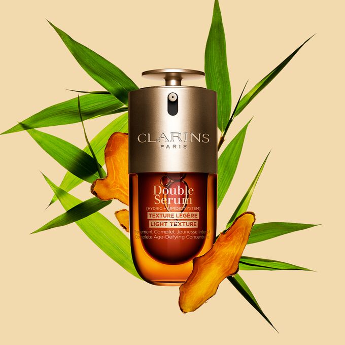 Un flacon de 30&nbsp;ml de Double Serum Light Texture de Clarins avec du curcuma et des feuilles de grand roseau de Provence sur un fond orange.